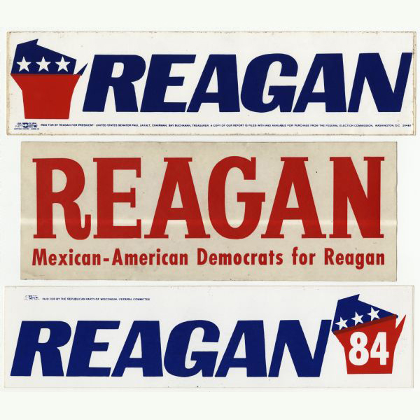 Three presidential political campaign bumper stickers for Ronald Reagan. The top bumper sticker has an image of the shape of the state of Wisconsin, which is split in half horizontally by a change in color, with the top in blue with white stars and the bottom in red. It reads: 'Reagan.' The middle bumper sticker has red text and reads: 'Reagan, 'Mexican-American Democrats for Reagan.' The bottom bumper sticker is white with blue text that reads: 'Reagan,' and on the right is an image of the shape of the state of Wisconsin, which is split in half horizontally by a change in color, with the top in blue with white stars and the bottom in red with white text that reads: '84.' 